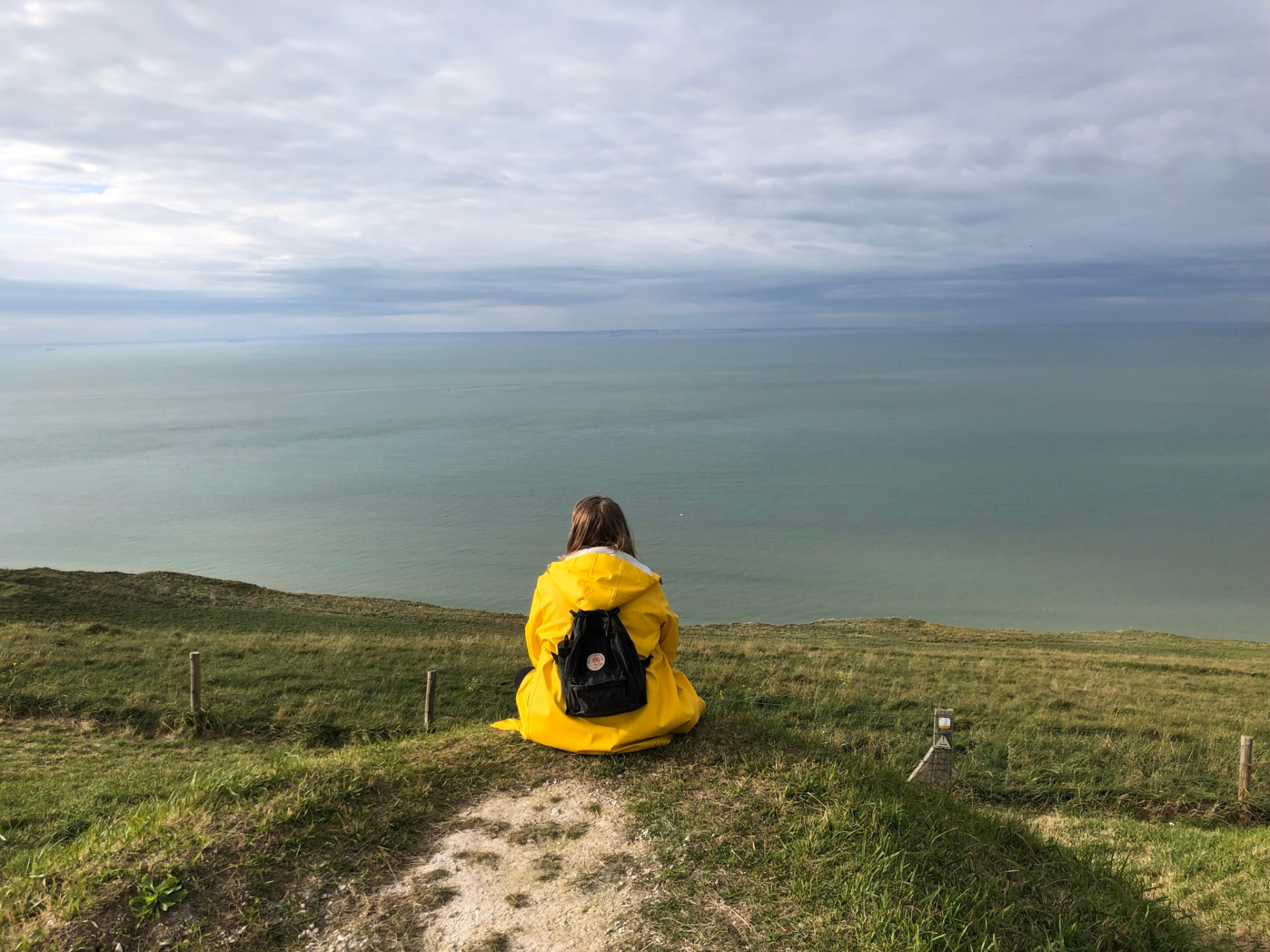 Zuzanna Lisowska sitting on a grassy cliff overlooking the ocean, wearing a yellow raincoat